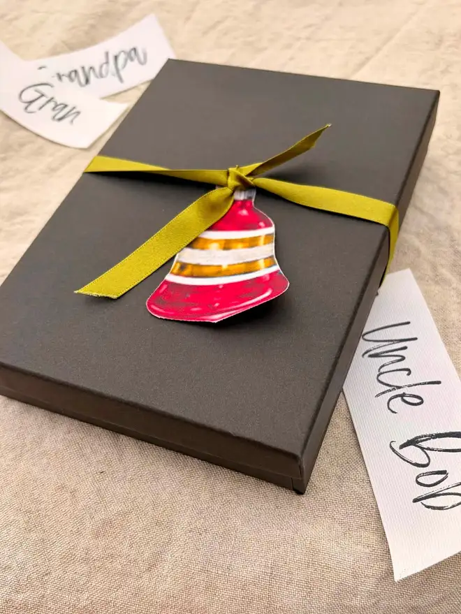 A slim black box tied with ribbon and a bell shaped bauble tag
