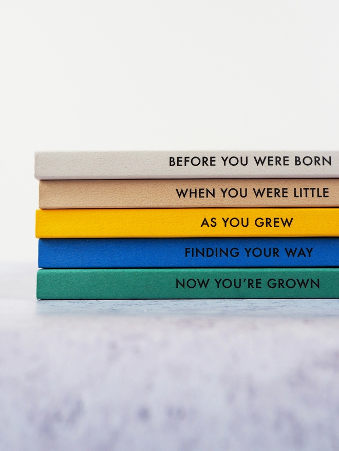 a stack of a gradient of colourful notebooks with personalised text down the spine
