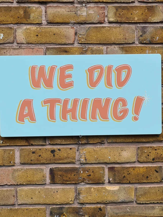 'We Did A Thing' Colourful Wedding Sign, a colourful wedding sign in blue with orange text, hung on a brick wall