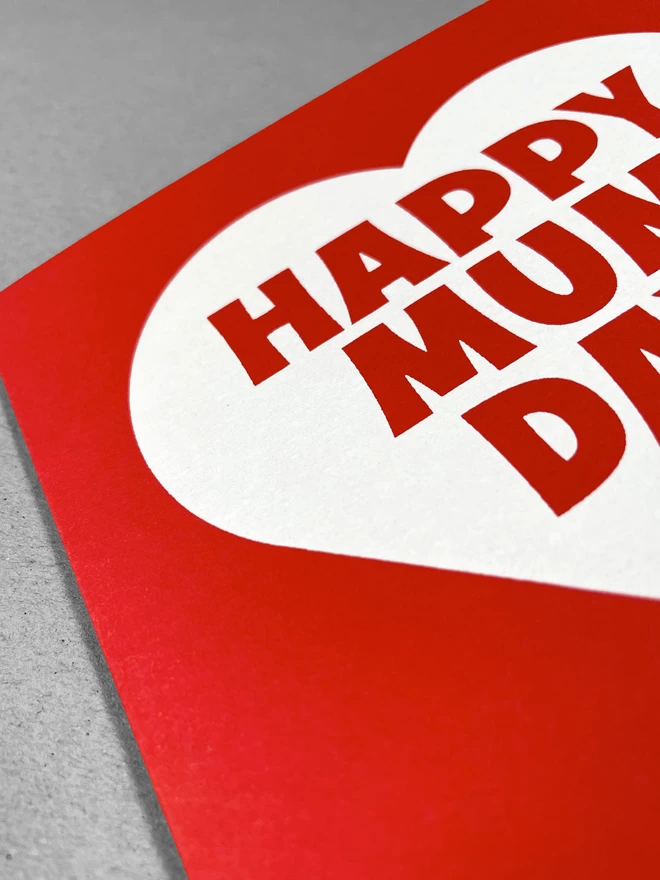 Close up of a red square card with a white heart, containing the words Mappy Mum Day - at a slight angle.