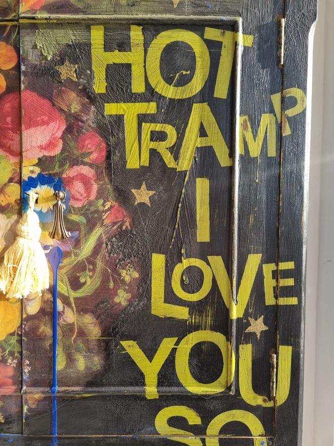 Elegant cocktail cabinet in black with colourful florals and text in chartreuse green that reads 'hot tramp, I love you so', a David Bowie lyric. Heavily distressed to age it. The interior is cobalt blue.