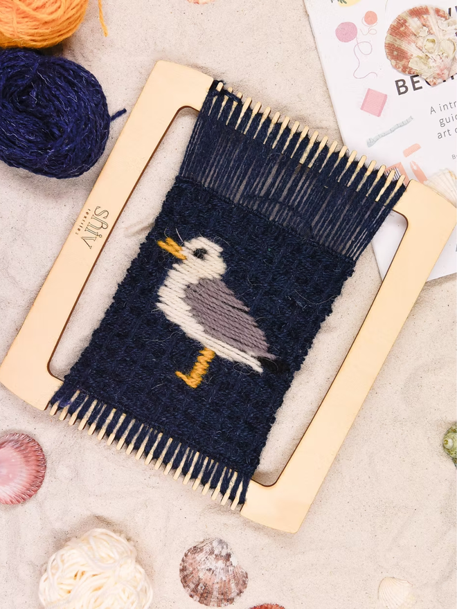 seaside weaving kit. a black weave piece with a seagull photographed on a loom.