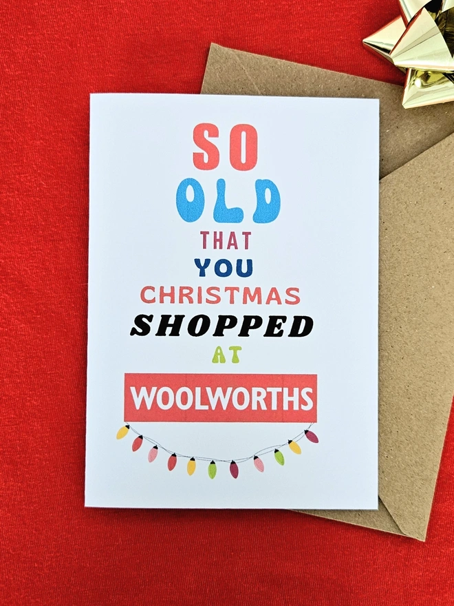 A photograph of the front of a humorous A6 greeting card illustrated using brightly coloured text and the retro shop logo. The text says so old you Christmas shopped at Woolworths with a colourful  string of fairy lights.