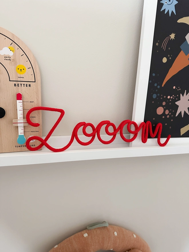 A zoom (with 3 os) sign in colour 'classic red' displayed on a shelf in a child's bedroom. 