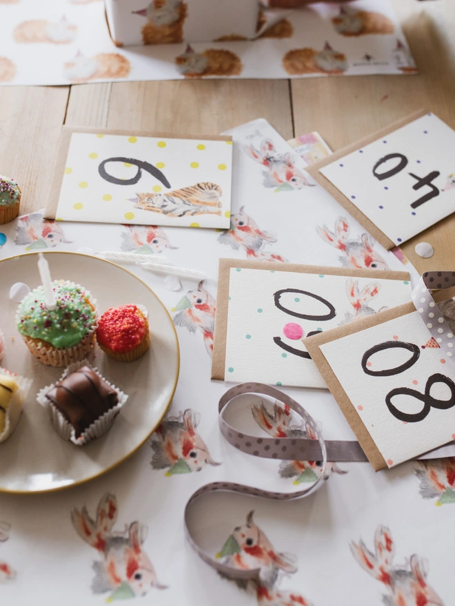 A Party Table Spread with Birthday Milestone Cards, Wrapping Paper and Cake 