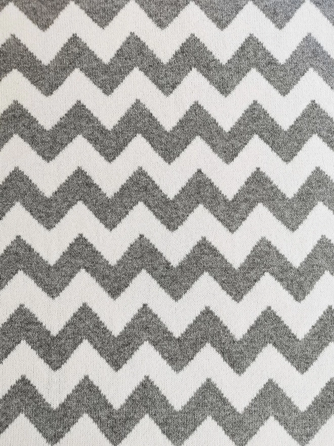 A close up of the pattern detail showing the reverse colourway of the knitted chevron blanket, white pattern on grey background.