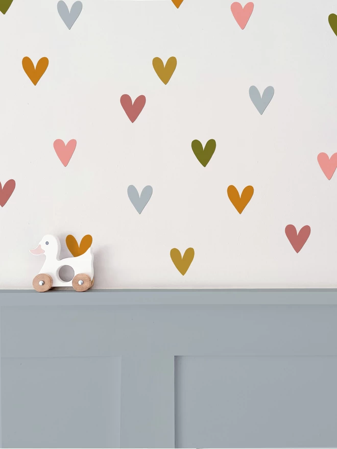 Heart shaped wall stickers in muted rainbow colours above duck egg blue wall panelling with wooden duck toy