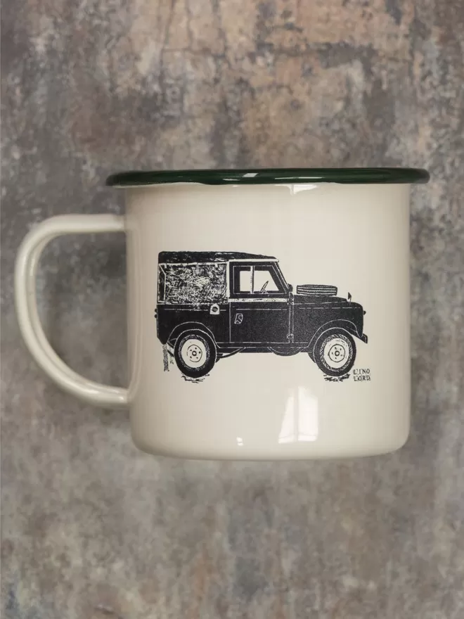 Picture of a Cream Enamel Mug with a Green Rim with a Land Rover design etched onto it, taken from an original Lino Print