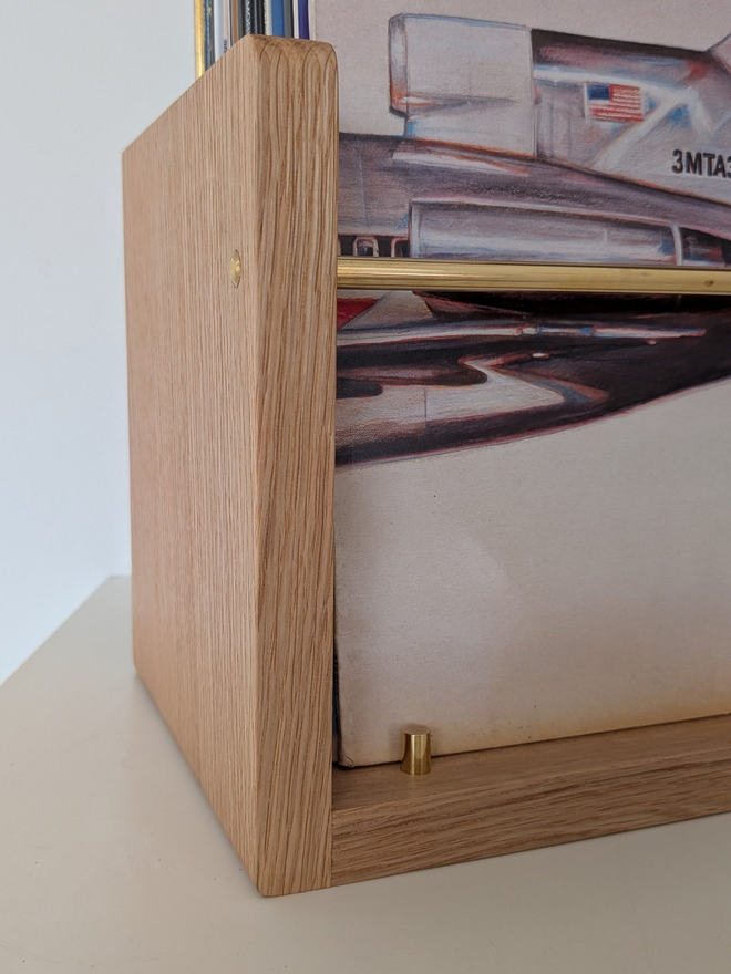 Close-up of the oak end panel, brass rod and brass base stop on a handmade vinyl record browser