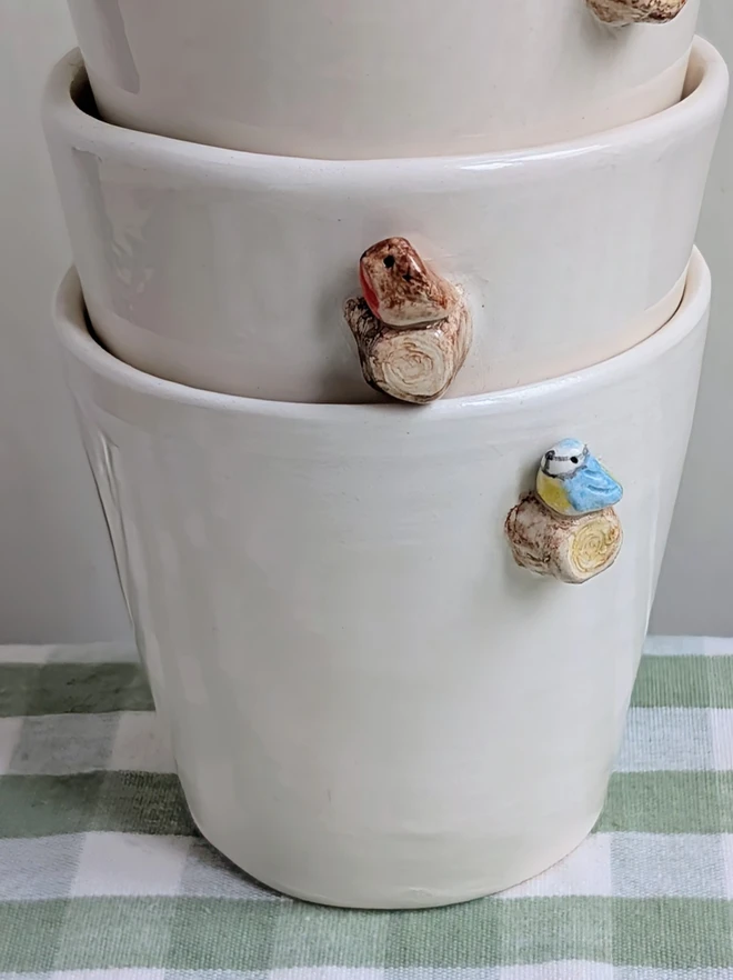 stacked robin and blue tit espresso coffee cups with a tiny handmade bird resting on a small ceramic tree branch in white earthenware pottery