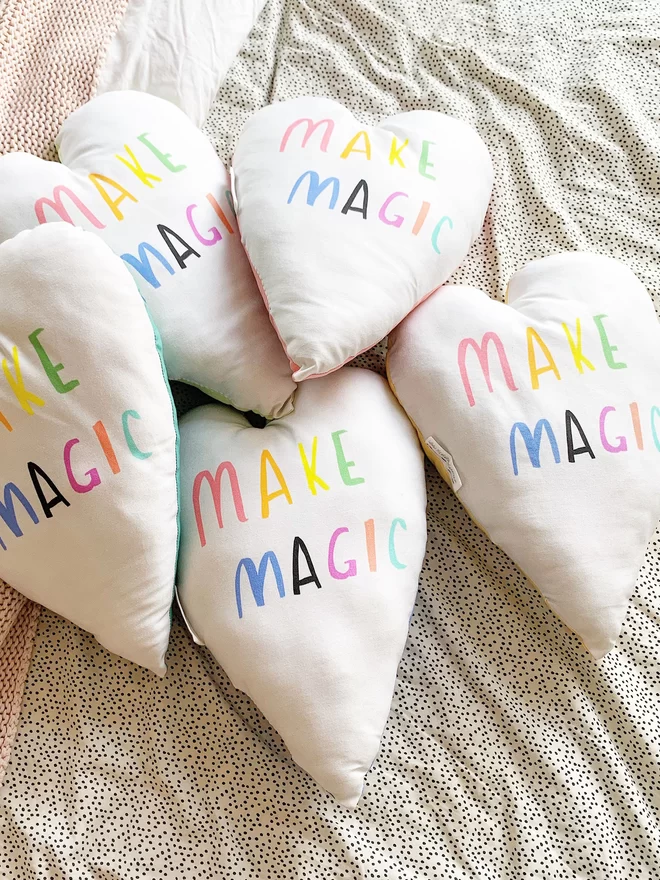 A pile of heart shaped cushions that all read 'MAKE MAGIC'
