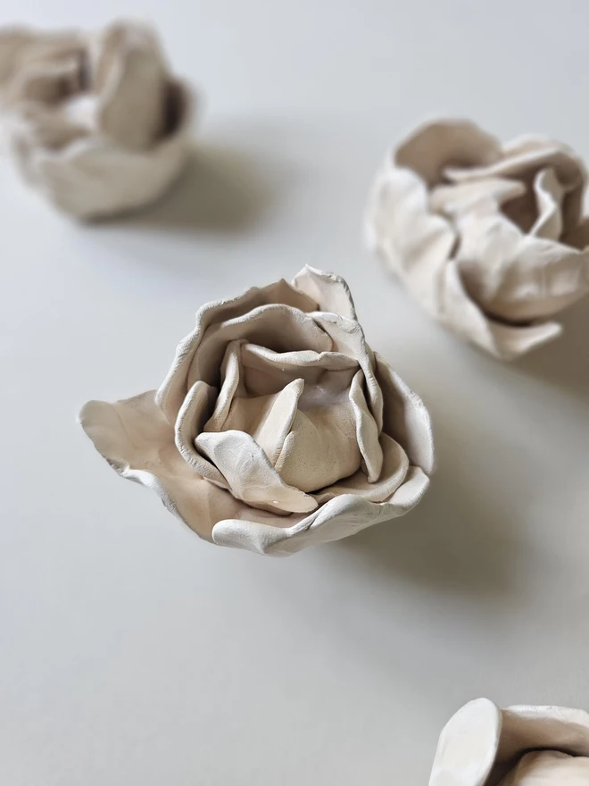 hand-sculpted ceramic flower in a soft cashmere glaze, featuring individually crafted petals and natural texture. Each unique piece is wall-mountable with a carved keyhole on the back