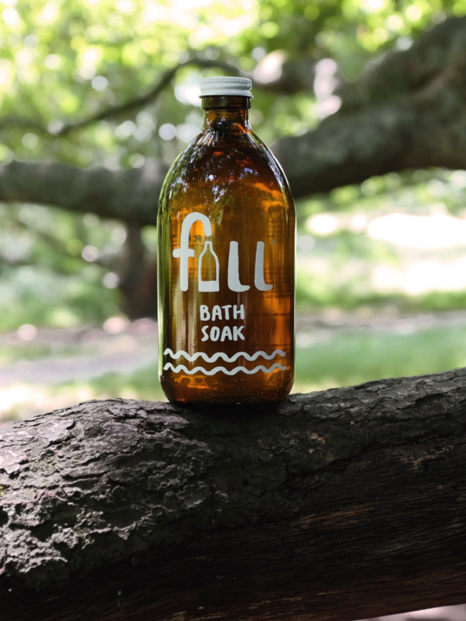 Bath Soak. An amber glass bottle on a wooden branch. The bottle reads Fill Bath Soak.