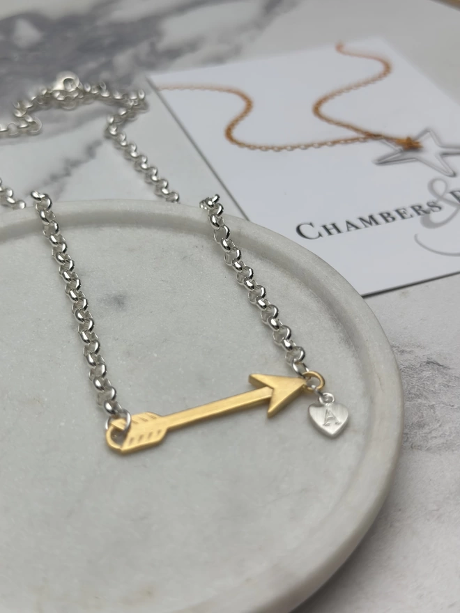 sterling silver chain with gold horizontal feather charm. a small silver heart charm hangs from the chain next to the feather