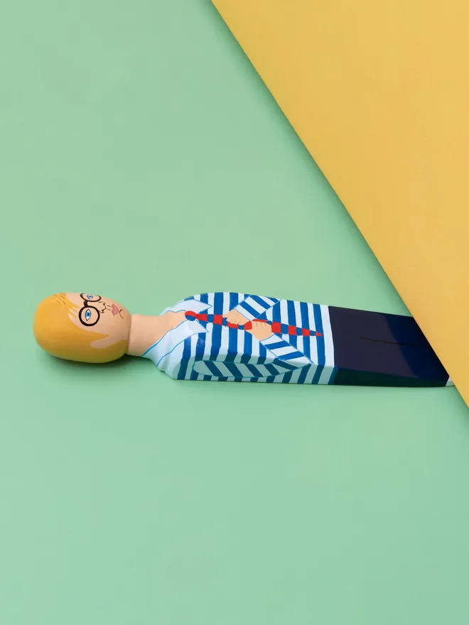 Wooden Door Stopper (Hock), a colourful wooden door stop sitting under a door. 