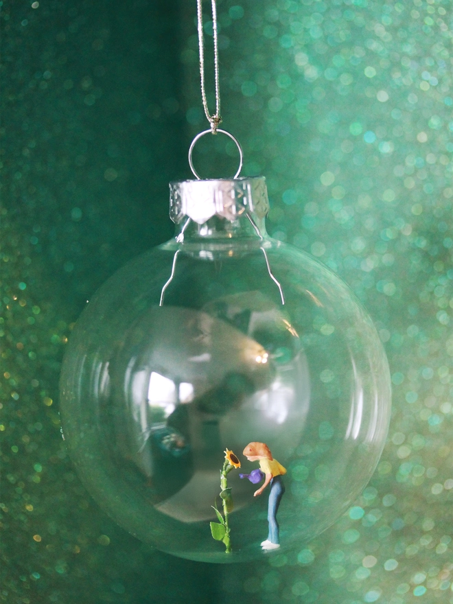 Miniature figure of a woman watering a sunflower in a glass Christmas bauble 