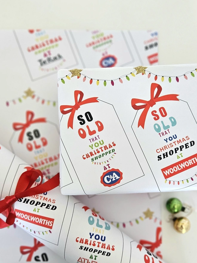 A photograph of a present wrapped in paper that has tags with a red bow printed on it. On each tag says so old that you Christmas shopped at Woolworths, Athena, C&A, Tie Rack, Sock Shop illustrated using brightly coloured text and the retro shop logo.