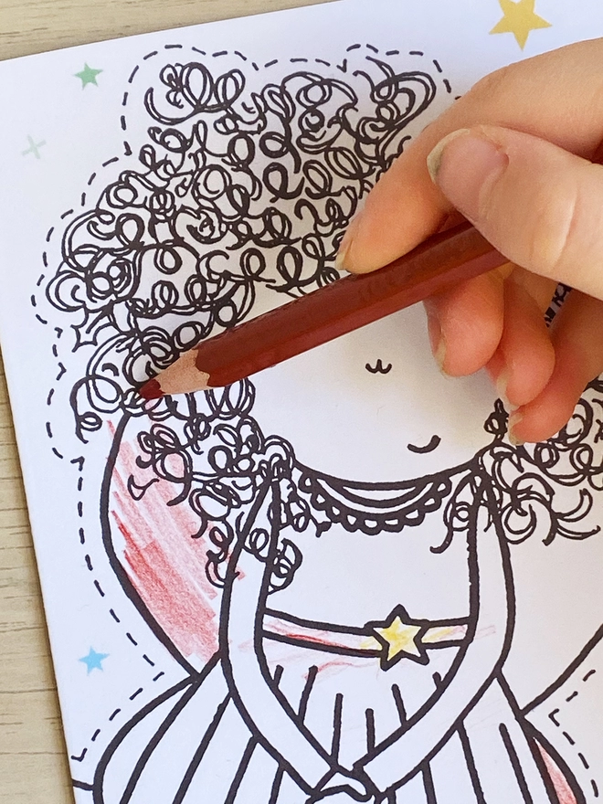 A child is colouring a Christmas greetings card with a fairy tree topper design.