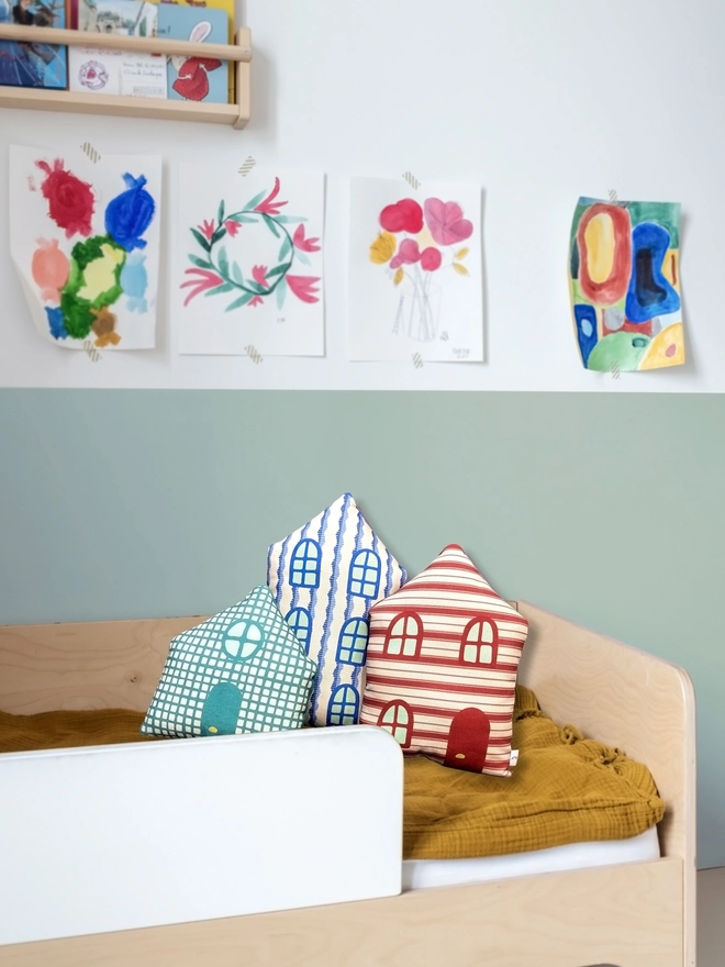 Set of 3 house cushions lying on a child's bed with a blue wall