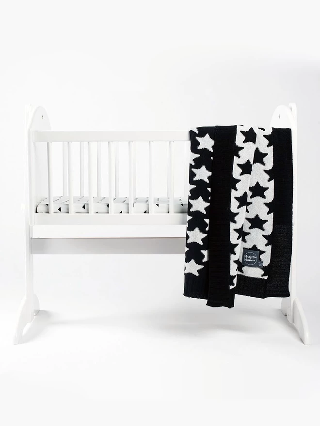 Black and white star pattern baby blanket draped over the side of a baby's crib.
