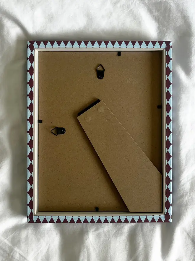 Burgundy & Blue Harlequin Frame, the back of a patterned colourful frame sitting on a plain white surface. 