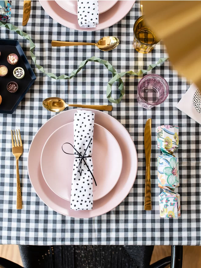 Place setting for Christmas table with pink plates, gold cutlery and paper origami crackers.