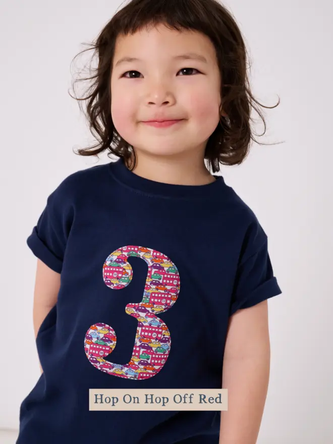  A 3 year old boy wearing a navy birthday t-shirt with a number 3 cut from liberty cars and london buses print on the front