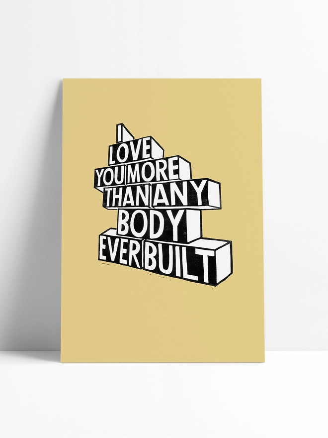 An unframed image of a pale yellow Woodism print in a limbo background. The typography is white out of black and reads: I Love You More Than Anybody Ever Built.