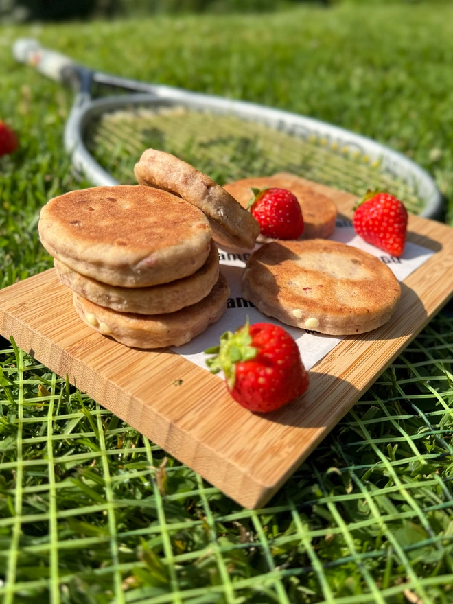 Stack of Strawberries & Cream Welsh Cakes with strawberries on a wooden board on a tennis racket on grass.