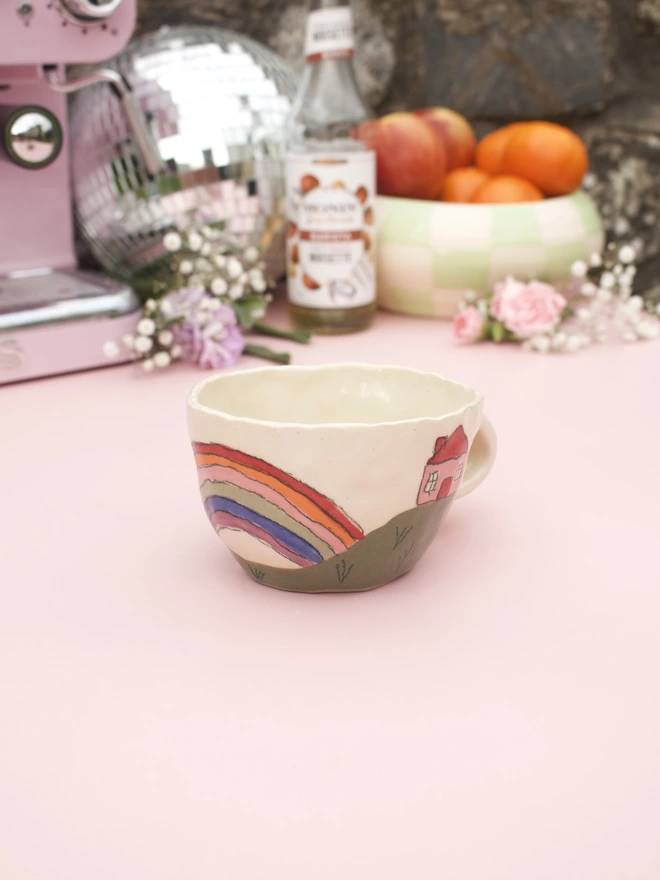handmade stoneware pottery mug decorated with a rainbow and house on a hill