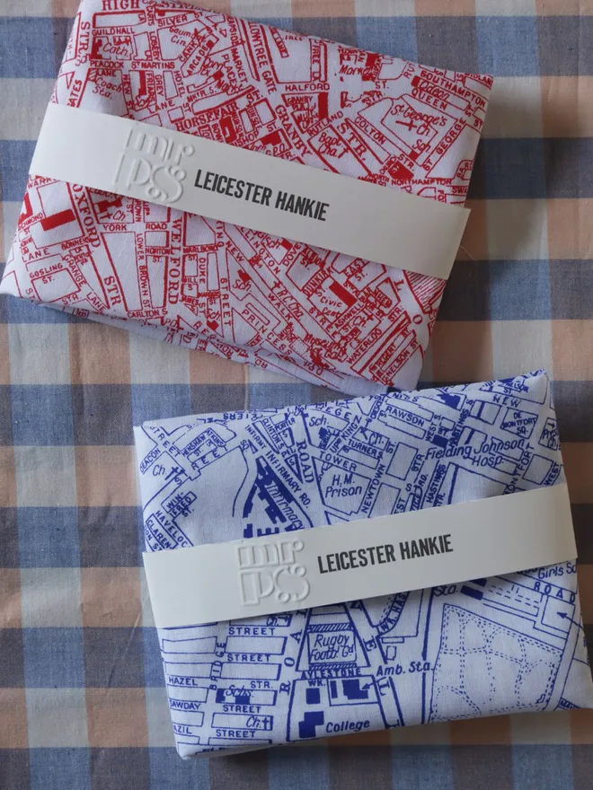 Two folded Mr.PS Leicester map printed handkerchiefs on a gingham tablecloth