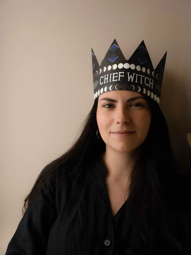 person wearingblack crown shaped card with 'chief witch' text