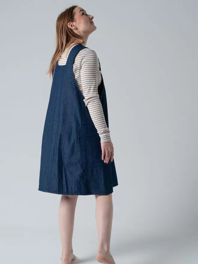Trapeze line denim pinafore dress with 2 large patch pockets. Back view studio.