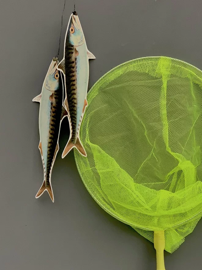 A sculptural wall hanging of two paper cut fish and a lime green fishing net against a grey painted wall