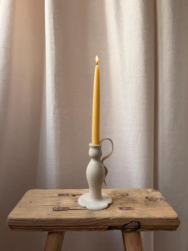 Clover Leaf candlestick with lit yellow candle, on wooden stool