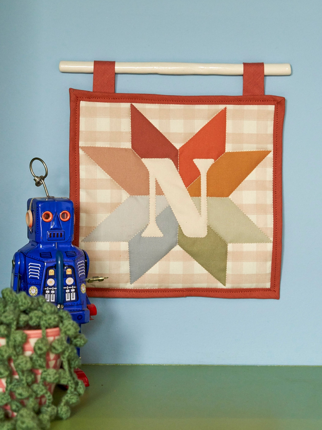 personalised initial quilt hanging. a hand-sewn hanging quilt with a star design in the centre, alongside the initial 'N'.