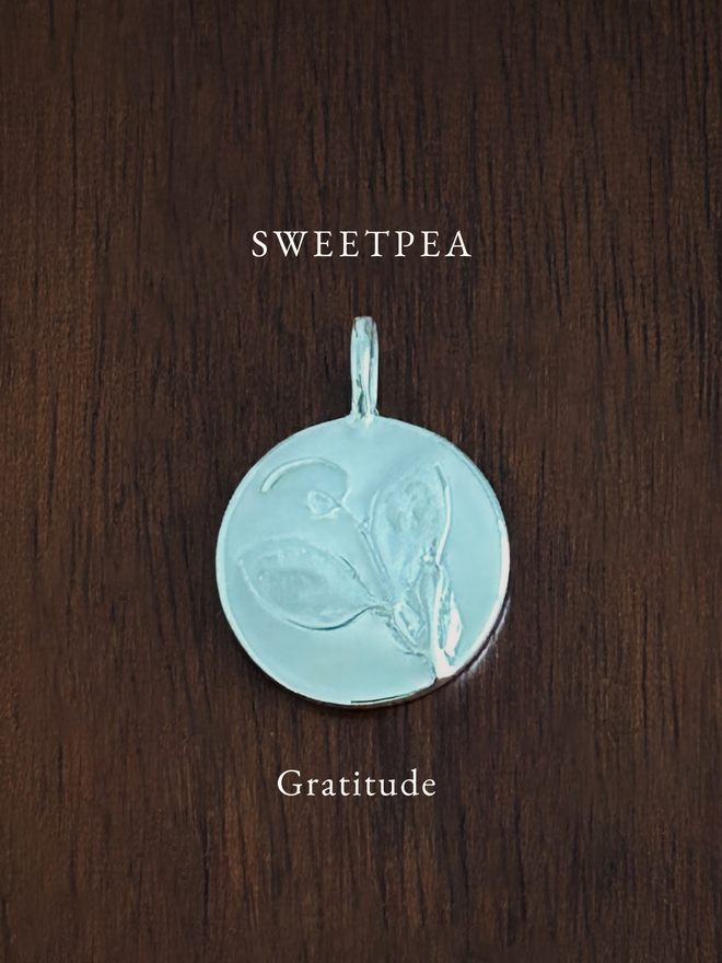 Sterling Silver Sweet Pea Coin Charm on a dark background with the language of flowers meaning, gratitude