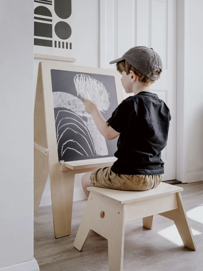 little boy drawing on the blackboard side of the easel.