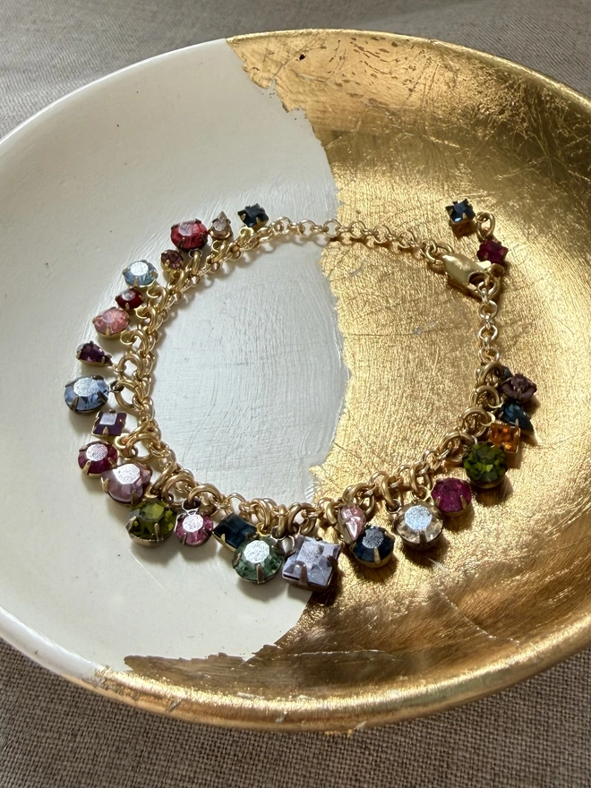 golden chain bracelet with rainbow jewel charms, sitting in gold and white dish