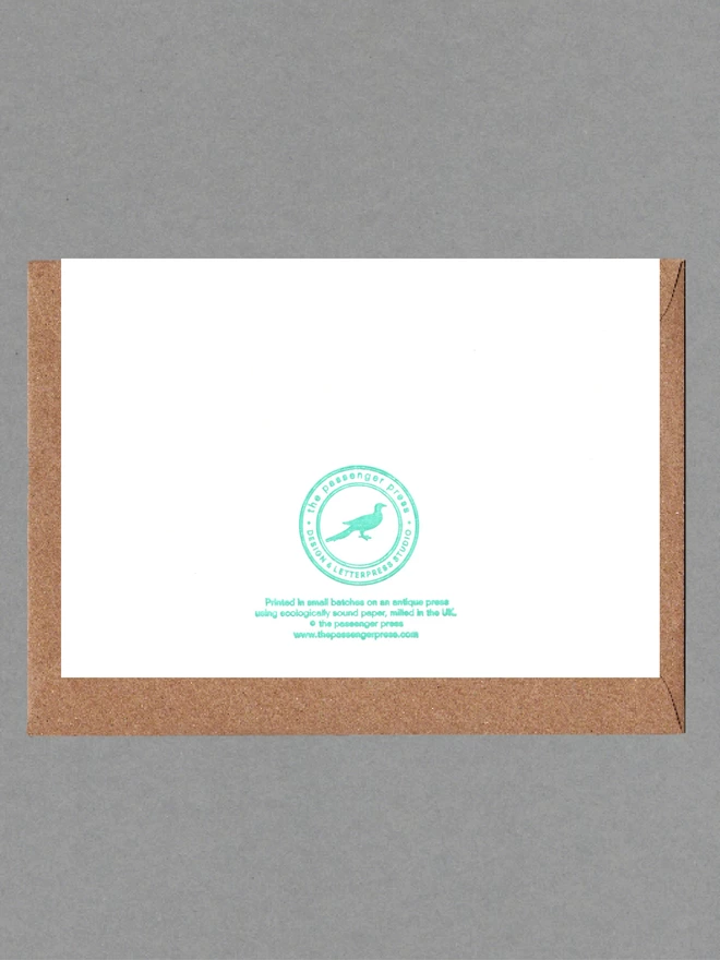 Back of white card with green text with brown envelope behind
