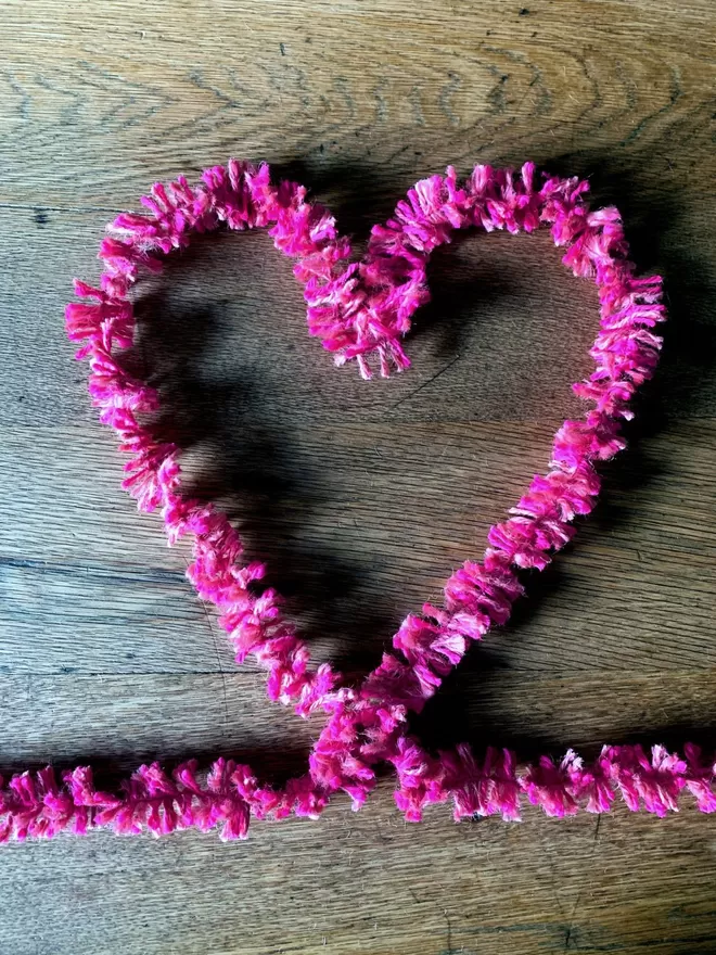 Bright pink jute string tinsel AKA Strinsel laid out in the shape of a heart on an oak table