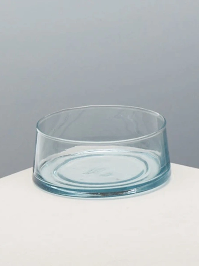 Low Glass Dish, a small glass dish sitting on a white counter top against a baby blue backdrop. 
