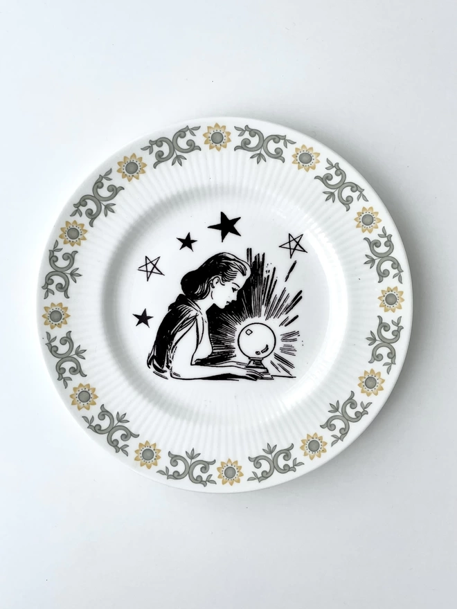 vintage plate with an ornate border, with a printed vintage illustration of a fortune teller looking in a crystal ball  in the middle 