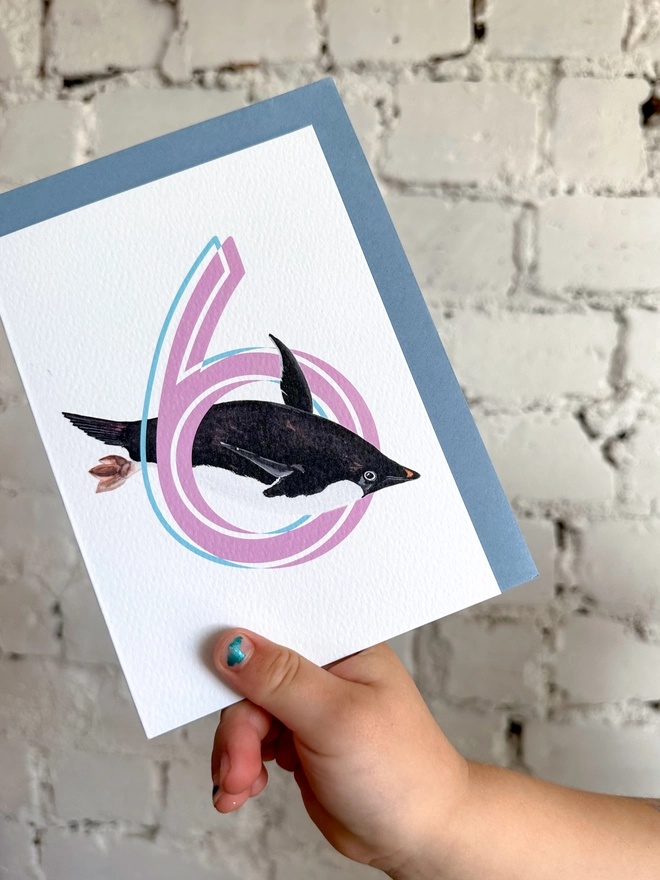 a white card with a big pink number 6 and an illustrated penguin with a blue envelope