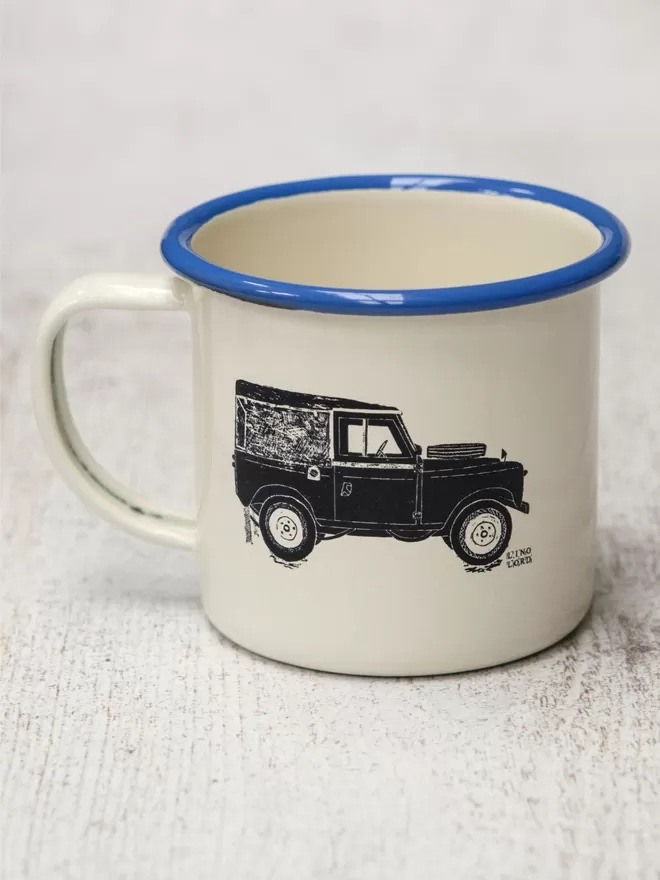 Picture of a Cream Enamel Mug with a Blue Rim with a Land Rover design etched onto it, taken from an original Lino Print