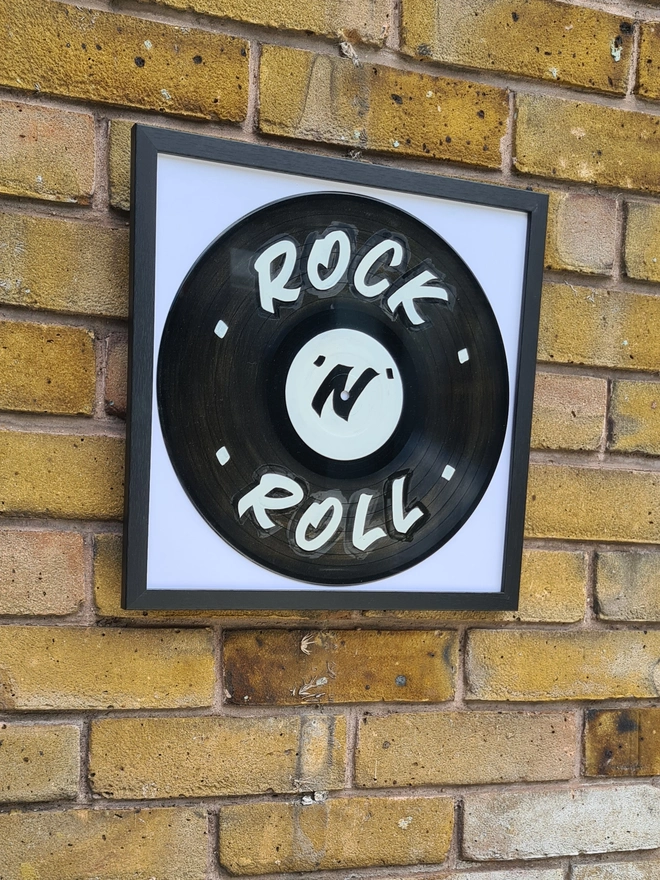 vinyl record with 'rock n roll' sign painting and black frame, hanging on brick wall