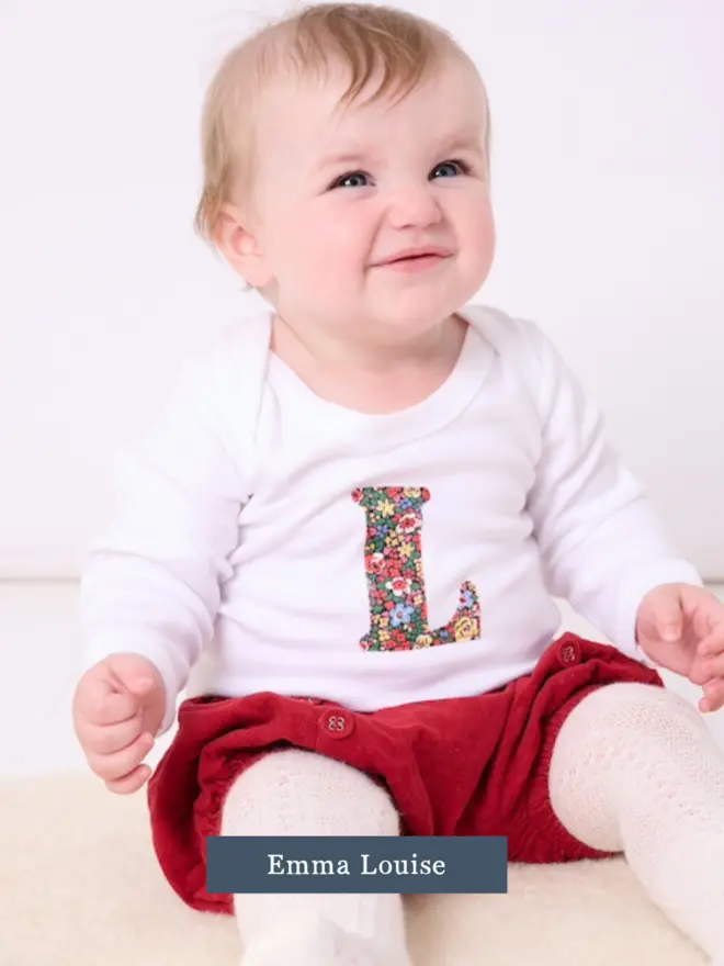 a baby wearing a personalised cotton bodysuit with her initial on in floral liberty print