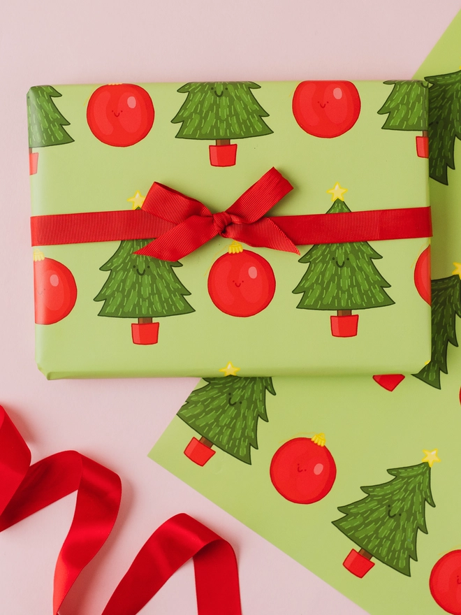 Green Christmas wrapping paper featuring a repeating pattern of hand-drawn Christmas trees with yellow stars and red Christmas baubles.