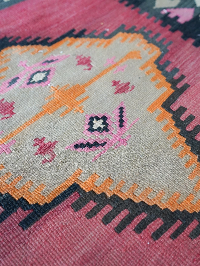 Orangey, red and black geometric vintage kilim hand woven rug on wooden floor in maximalist dining room with green woodwork