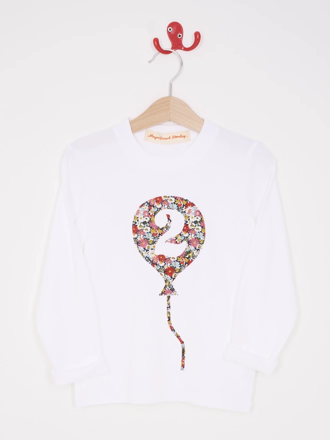 A white cotton long sleeve t-shirt. The t-shirt features a balloon with the number 2 cut out from it, appliquéd in a floral Liberty print.